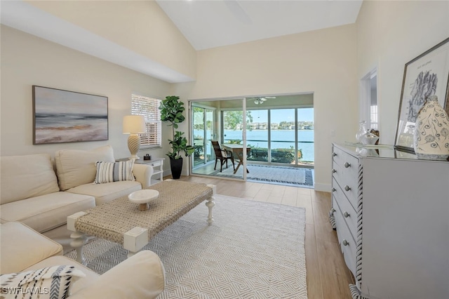 living area featuring high vaulted ceiling, a water view, light wood-type flooring, and a wealth of natural light