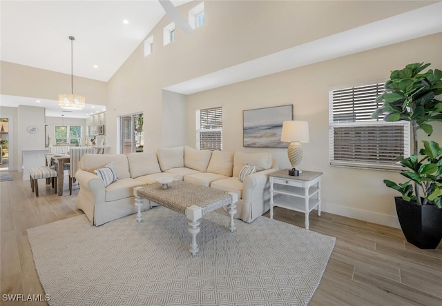 living room featuring wood finished floors, baseboards, high vaulted ceiling, recessed lighting, and a notable chandelier