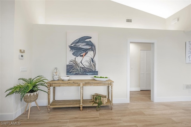 hall with baseboards, vaulted ceiling, wood finished floors, and visible vents