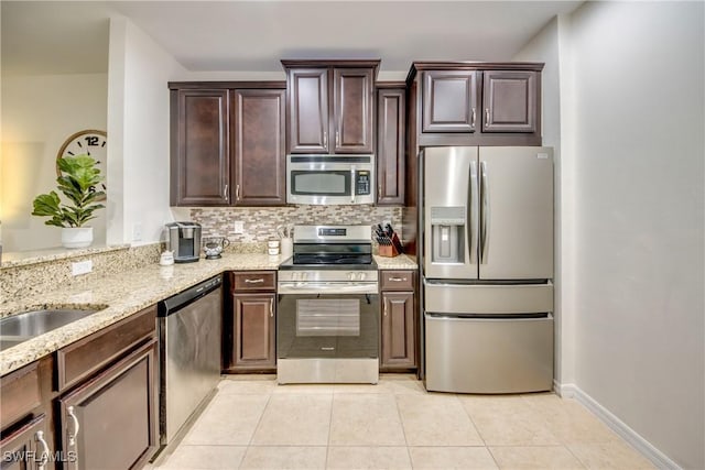 kitchen with light tile patterned flooring, light stone countertops, dark brown cabinets, stainless steel appliances, and decorative backsplash