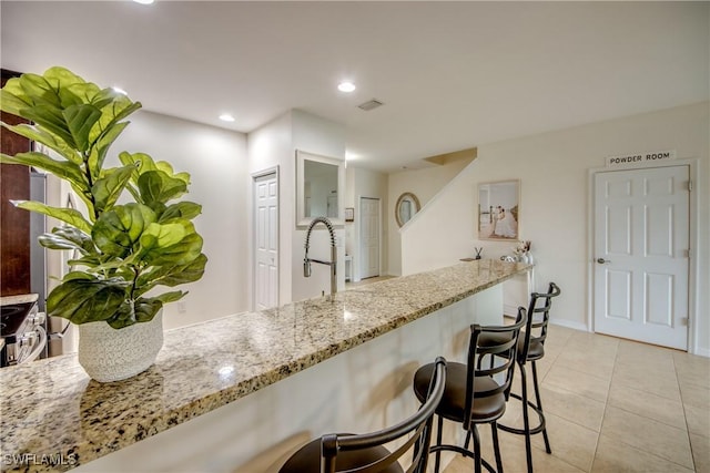 kitchen with light stone counters, a sink, light tile patterned floors, a kitchen bar, and visible vents
