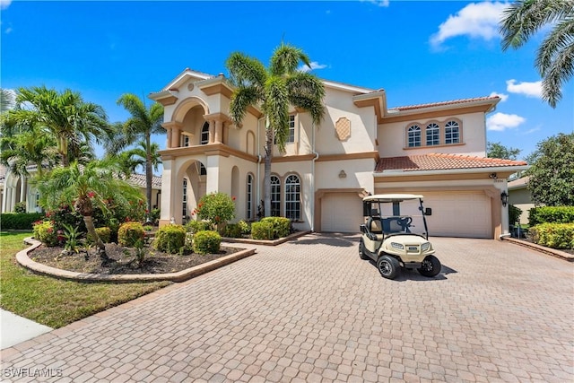 mediterranean / spanish-style house featuring decorative driveway, an attached garage, a tiled roof, and stucco siding
