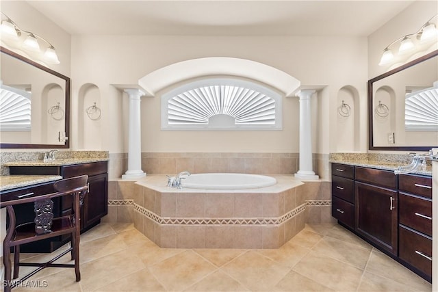 bathroom with a garden tub, tile patterned flooring, two vanities, and ornate columns