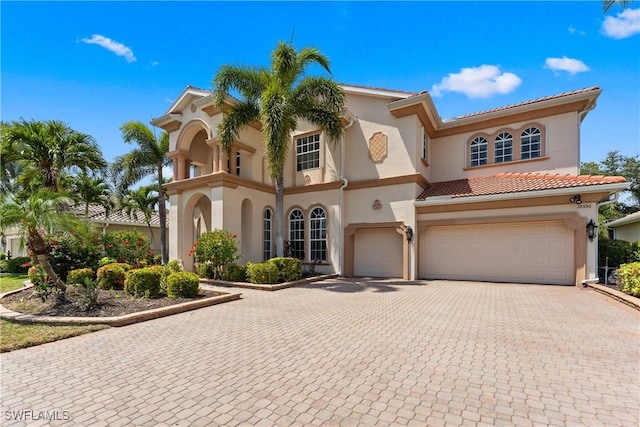 mediterranean / spanish-style home featuring decorative driveway, stucco siding, a tiled roof, and a garage
