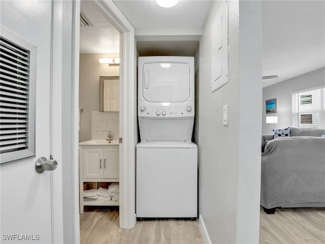 laundry area with light wood-style floors, laundry area, baseboards, and stacked washing maching and dryer