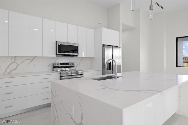 kitchen featuring an island with sink, appliances with stainless steel finishes, a sink, white cabinetry, and modern cabinets