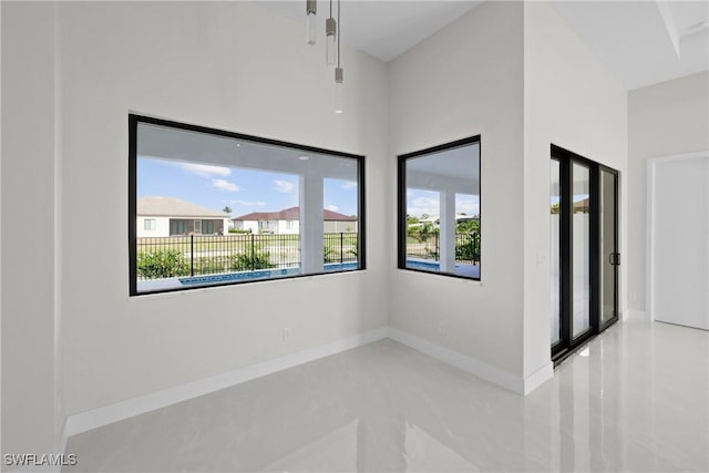tiled empty room with a towering ceiling, a healthy amount of sunlight, and baseboards