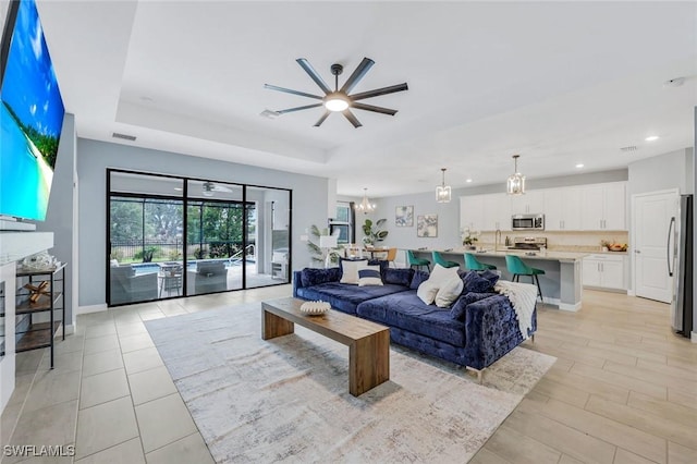living area featuring visible vents, baseboards, ceiling fan with notable chandelier, a tray ceiling, and recessed lighting