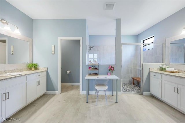 full bath with baseboards, two vanities, a stall shower, and visible vents