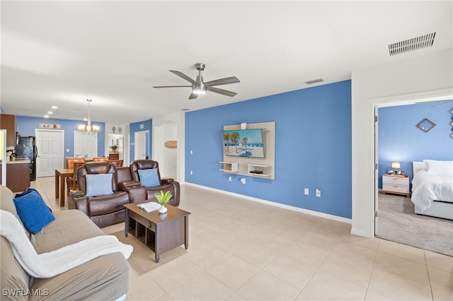 living area featuring light tile patterned flooring, baseboards, visible vents, and ceiling fan with notable chandelier