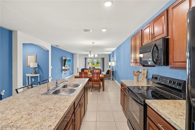 kitchen with brown cabinets, light tile patterned flooring, an inviting chandelier, a sink, and black appliances