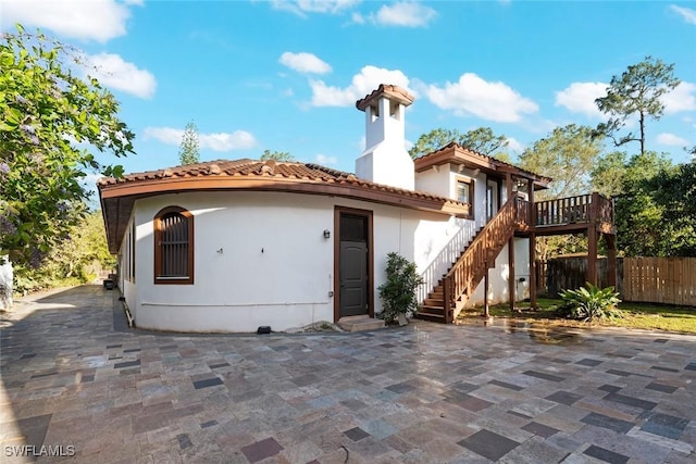 view of front of home featuring a tile roof, fence, a patio, stairs, and stucco siding