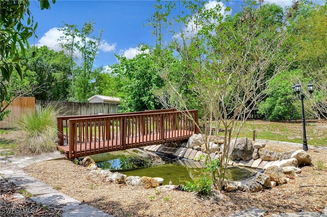 view of community with fence, a wooden deck, and a small pond