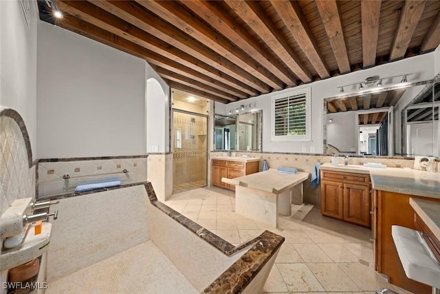 bathroom with beam ceiling, tile walls, a wainscoted wall, two vanities, and a stall shower