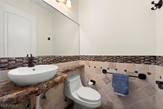 half bathroom with a sink, a wainscoted wall, toilet, and tile walls