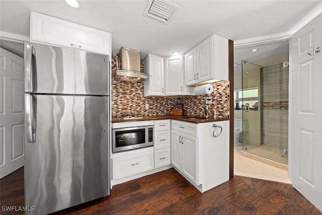 kitchen featuring visible vents, wall chimney exhaust hood, white cabinets, and stainless steel appliances