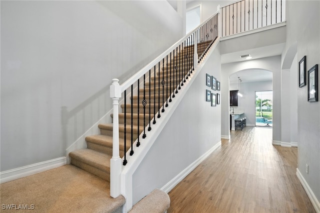 stairway with baseboards, arched walkways, a high ceiling, and wood finished floors