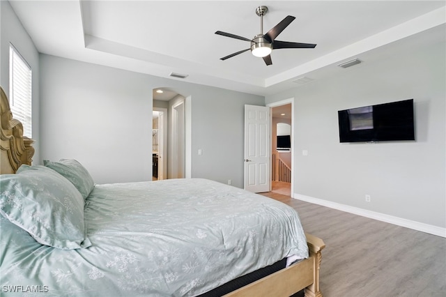 bedroom with arched walkways, visible vents, wood finished floors, and a tray ceiling