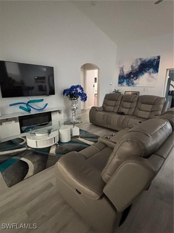 living area featuring arched walkways, wood finished floors, and lofted ceiling