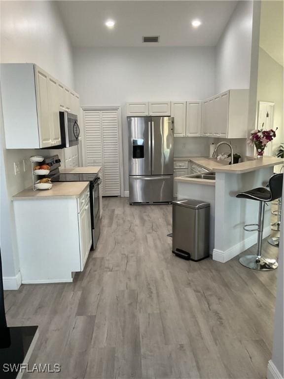 kitchen with appliances with stainless steel finishes, light wood-style flooring, a peninsula, a kitchen bar, and visible vents