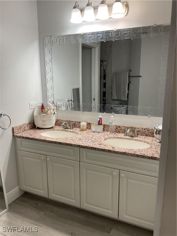 bathroom with double vanity, a sink, baseboards, and wood finished floors