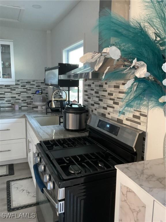 kitchen featuring a sink, white cabinets, stainless steel gas range oven, and tasteful backsplash