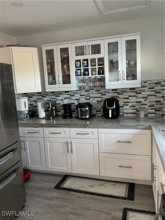 bar featuring tasteful backsplash, freestanding refrigerator, and light wood-type flooring