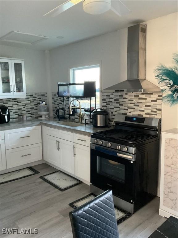kitchen with wall chimney range hood, stainless steel gas range, light wood finished floors, and a sink