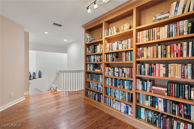 sitting room with visible vents, bookshelves, wood finished floors, and an upstairs landing
