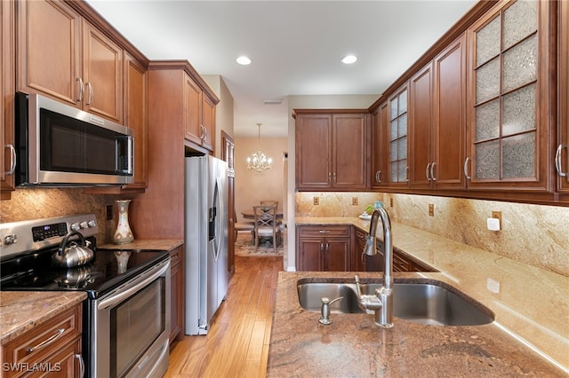 kitchen with brown cabinetry, light stone countertops, light wood-type flooring, a sink, and stainless steel appliances