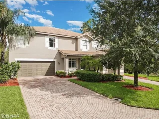 view of front of property with stucco siding, a tiled roof, decorative driveway, a front lawn, and an attached garage