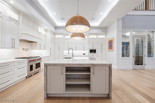 188 W St, Naples, FL 34108 - kitchen with range with two ovens, a sink, a raised ceiling, light wood-style floors, and glass insert cabinets