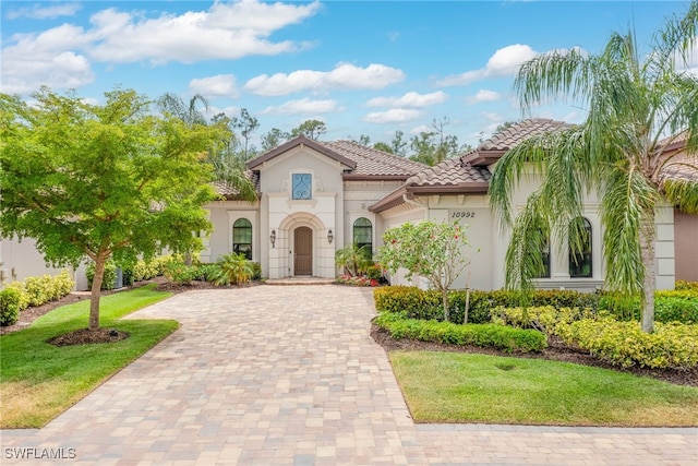 mediterranean / spanish house with a front yard, stucco siding, a tiled roof, and decorative driveway