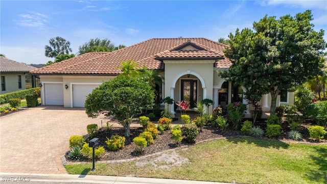 mediterranean / spanish-style home featuring decorative driveway, an attached garage, a tile roof, and stucco siding