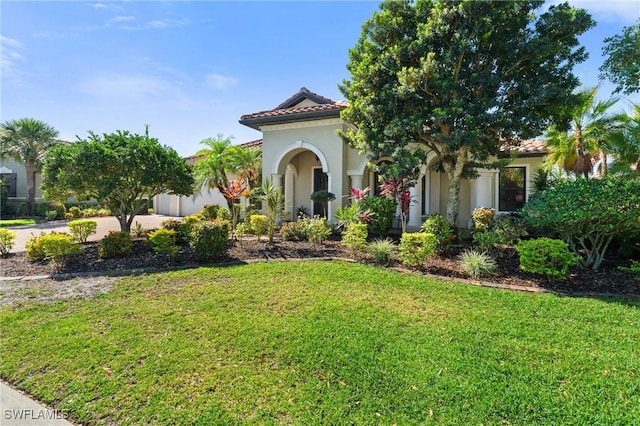 mediterranean / spanish house featuring a tiled roof, stucco siding, and a front lawn