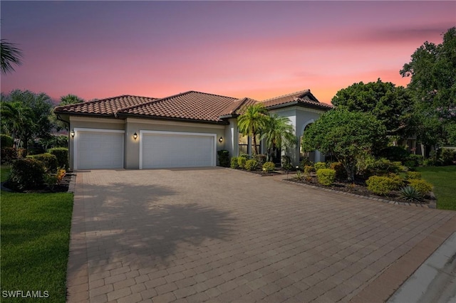 mediterranean / spanish home with a tiled roof, a garage, decorative driveway, a yard, and stucco siding