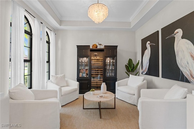 living area featuring an inviting chandelier, a raised ceiling, and ornamental molding