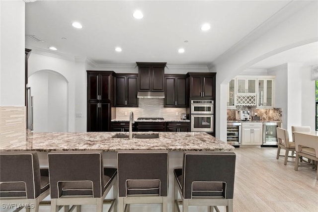 kitchen featuring a sink, arched walkways, a kitchen breakfast bar, and beverage cooler