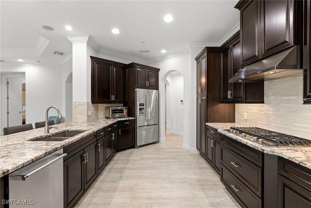 kitchen featuring arched walkways, a sink, appliances with stainless steel finishes, and light stone countertops