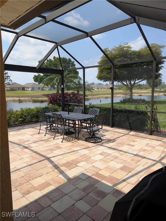 view of patio / terrace featuring glass enclosure, outdoor dining area, and a water view
