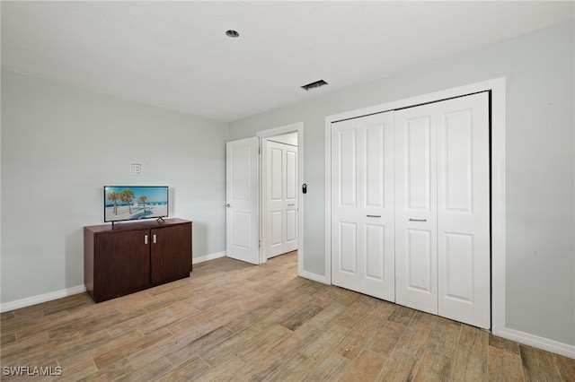 unfurnished bedroom with baseboards, a closet, wood finished floors, and visible vents