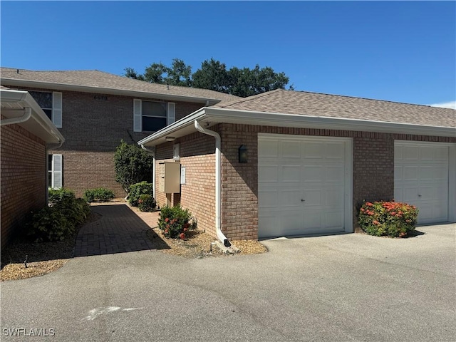view of front of house with driveway, an attached garage, a shingled roof, and brick siding