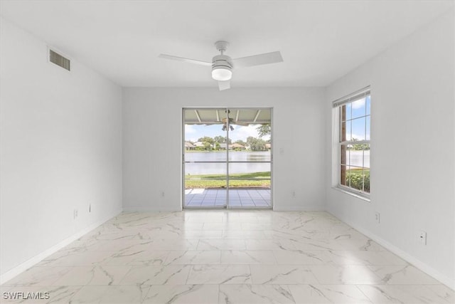 unfurnished room with visible vents, a water view, baseboards, a ceiling fan, and marble finish floor