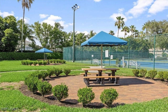 view of property's community with a tennis court, fence, and a lawn