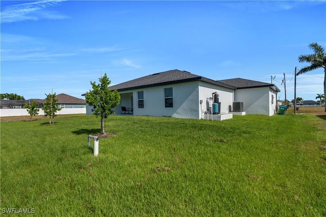 rear view of house with stucco siding, a lawn, and central AC unit