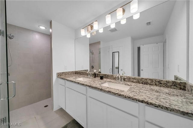 bathroom with tile patterned floors, a tile shower, double vanity, and a sink