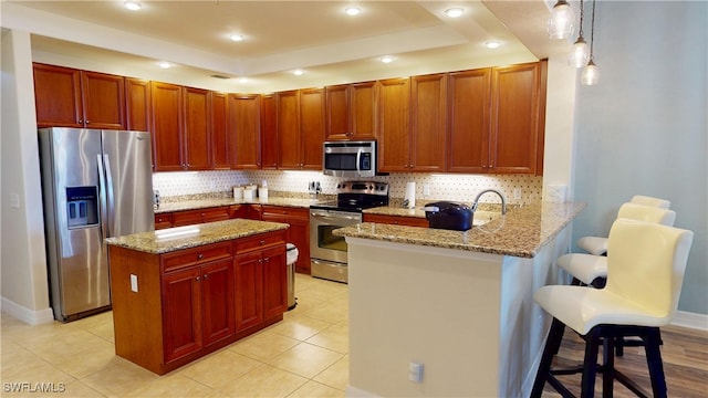 kitchen featuring light stone countertops, appliances with stainless steel finishes, a peninsula, backsplash, and a tray ceiling