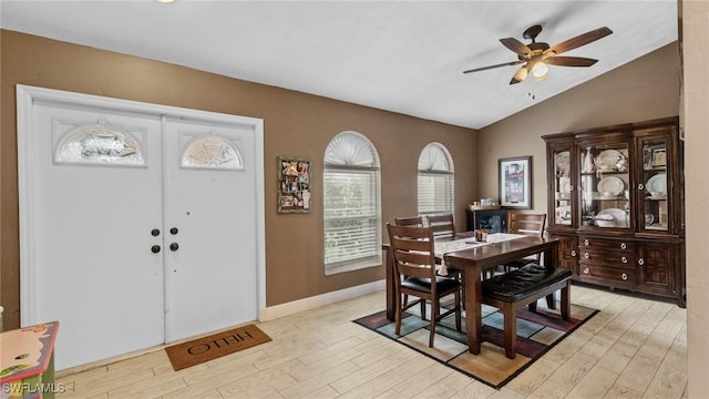 dining area featuring baseboards, ceiling fan, vaulted ceiling, and light wood-style flooring