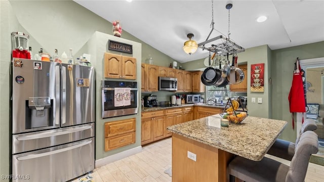 kitchen with appliances with stainless steel finishes, light stone counters, lofted ceiling, and light wood-style floors