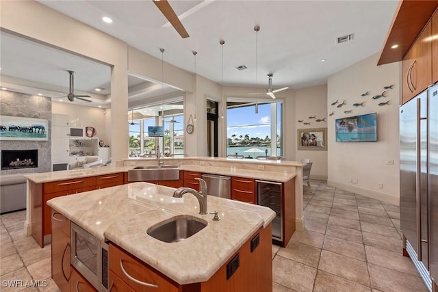 kitchen with a sink, an island with sink, a ceiling fan, stainless steel appliances, and wine cooler